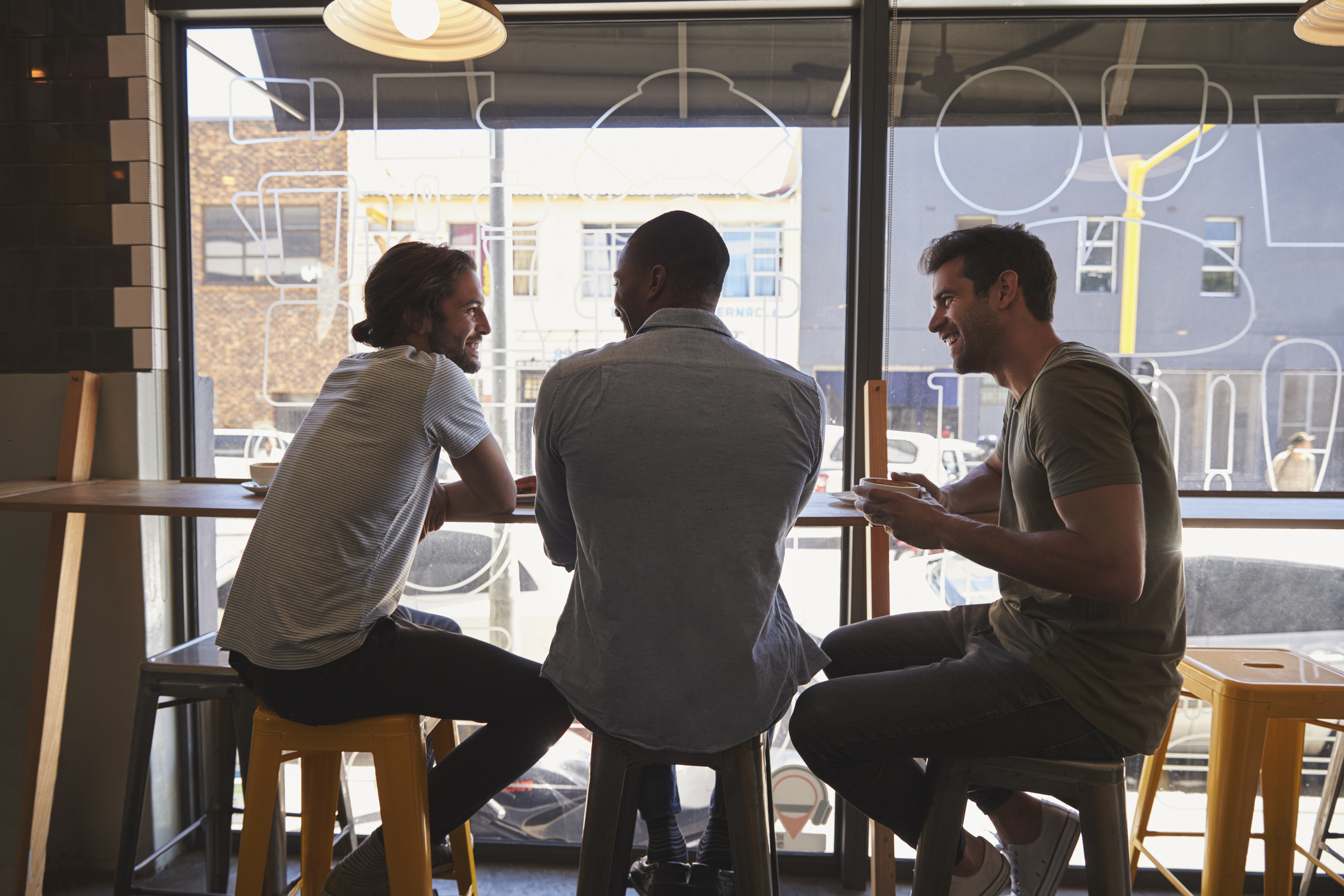 Rear View Of Three Male Friends Meeting In Coffee Shop Three men sitting and talking at a table
